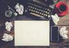 Ein leeres Blatt Papier auf dem Schreibtisch eines Autors, zusammen mit einer Schreibmaschine, Entwürfen, Handy, Kamera und einem Kaffee